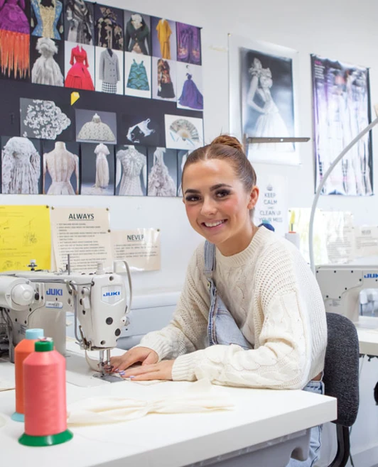 A student smiling while working on a sewing machine in the fashion design studio at Glasgow Kelvin College A student smiling while working on a sewing machine in the fashion design studio at Glasgow Kelvin College